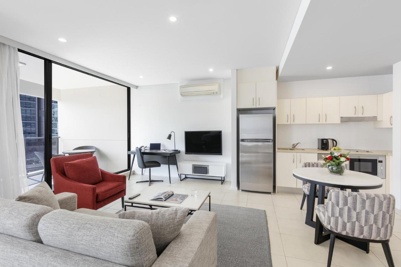 Meriton Suites Kent Street, Sydney Exterior photo The photo shows a modern living space that features an open-plan layout. On one side, there is a cozy gray sofa and a red armchair, creating a comfortable seating area. A small coffee table is positioned in front of the sofa. 

Adjacent to this seati