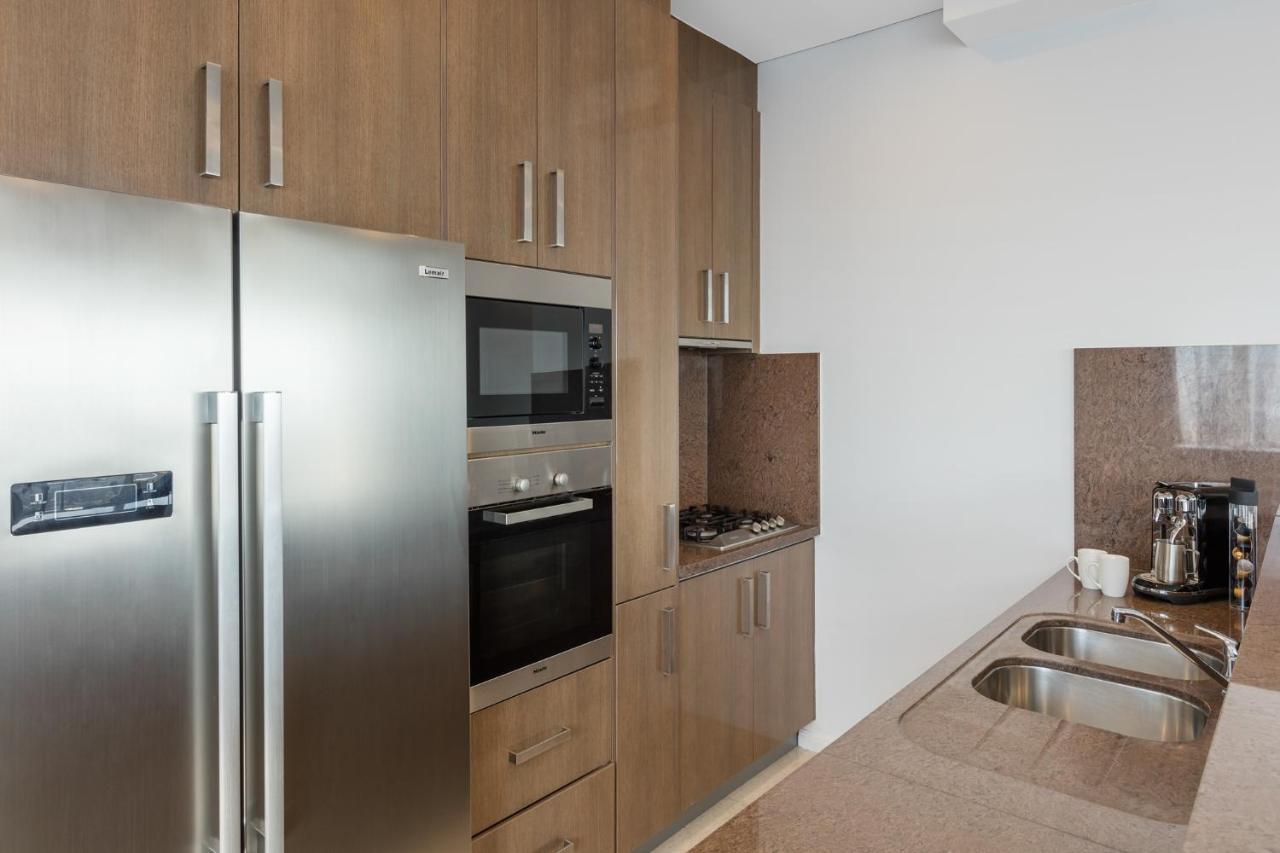 Meriton Suites Kent Street, Sydney Exterior photo The photo shows a modern kitchen featuring a combination of appliances and cabinetry. On the left, there is a stainless steel refrigerator. Next to it, built into the cabinetry, is an oven and a microwave. The countertop is smooth and made of a light
