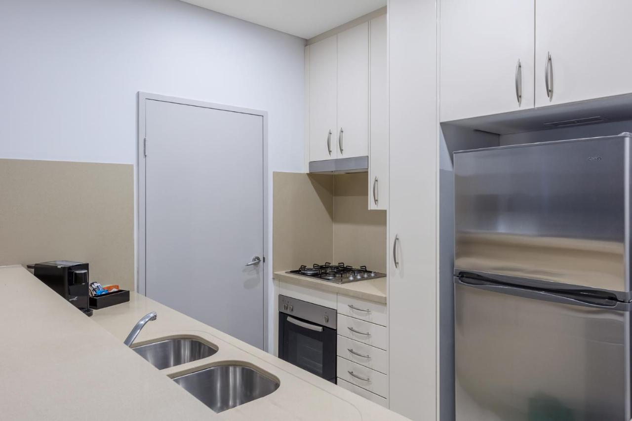 Meriton Suites Kent Street, Sydney Exterior photo The photo shows a modern kitchen featuring a sleek design. It includes a light-colored countertop with a double sink, a gas stove, and an oven integrated into the cabinetry. There are upper cabinets for storage, and a stainless-steel refrigerator is 
