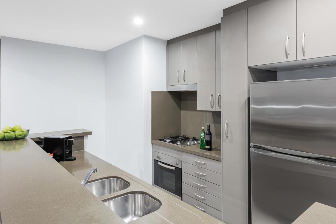 Meriton Suites Kent Street, Sydney Exterior photo The photo depicts a modern kitchen featuring a compact design. It includes gray cabinetry with several drawers and cabinets, a countertop with two sinks, and stainless steel appliances. There is a stove and oven integrated into the cabinetry, along w