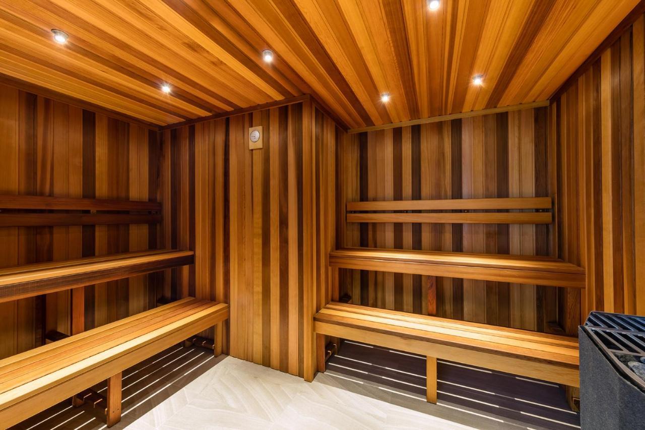 Meriton Suites Kent Street, Sydney Exterior photo The photo depicts the interior of a sauna. The walls and benches are made of wood, featuring a warm, natural finish with horizontal and vertical wood paneling. There are multiple levels of benches for seating, and the space is illuminated by recessed